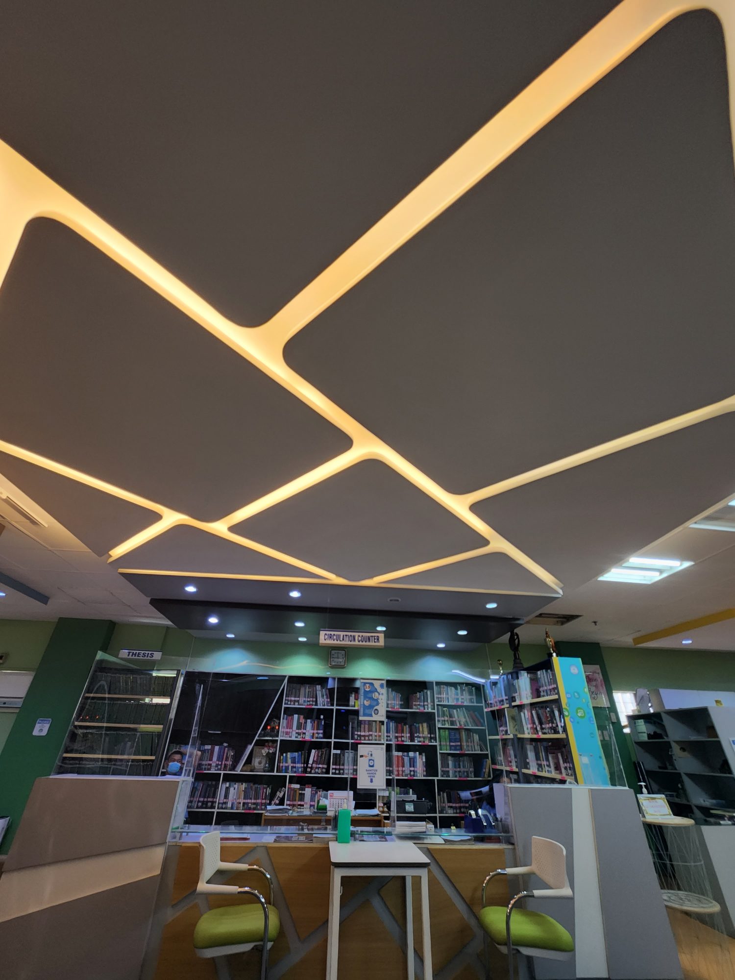 Dramatic angular LED-strip ceiling above green-walled library stacks