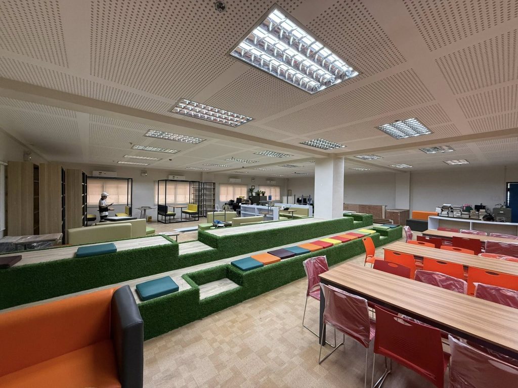 Bright reading room with green tiered steps and orange chairs at group tables