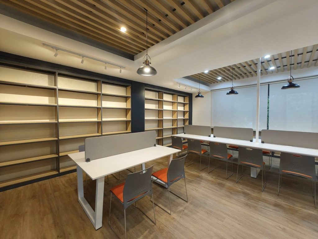 Study tables beneath a warm wood-slat ceiling beside new shelving