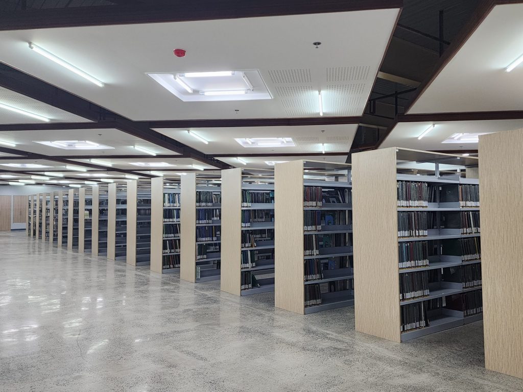 Aisle of tall library stacks under a warm slatted ceiling