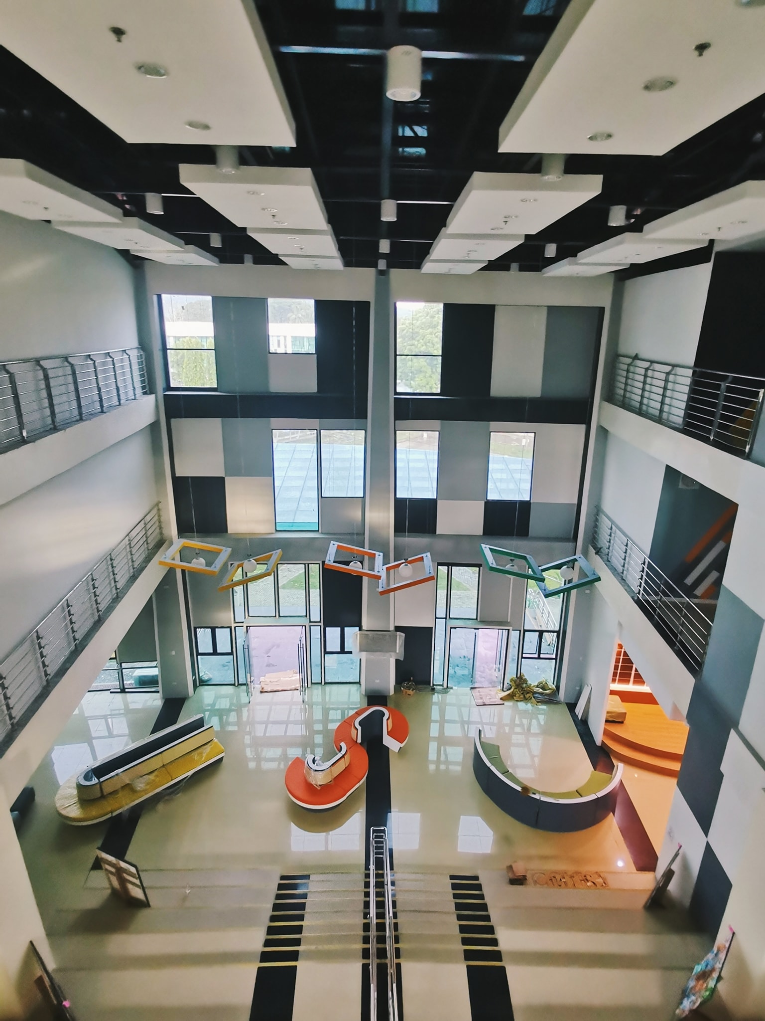 Double-height atrium with tall windows and orange seating pods